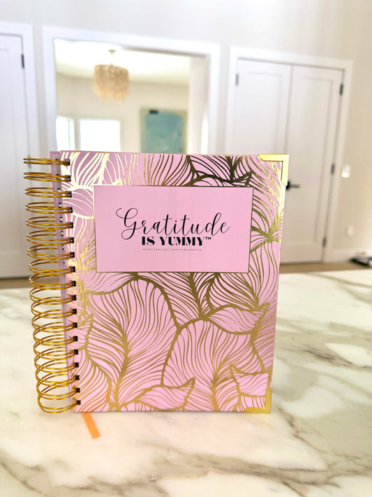 Gratitude is Yummy Journal on a marble desk with pink flowers for a morning manifestation ritual