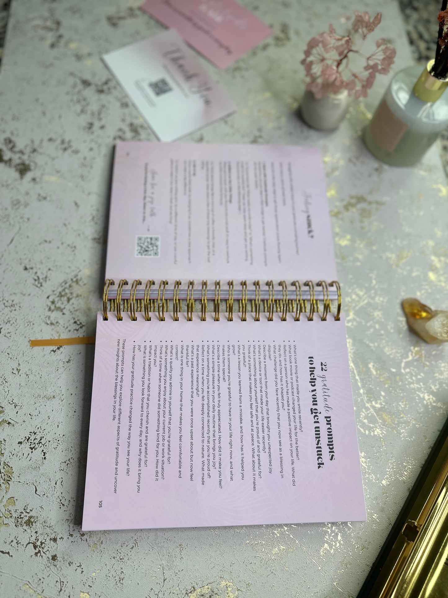 Open notebook on a decorative surface with flowers and a bottle.