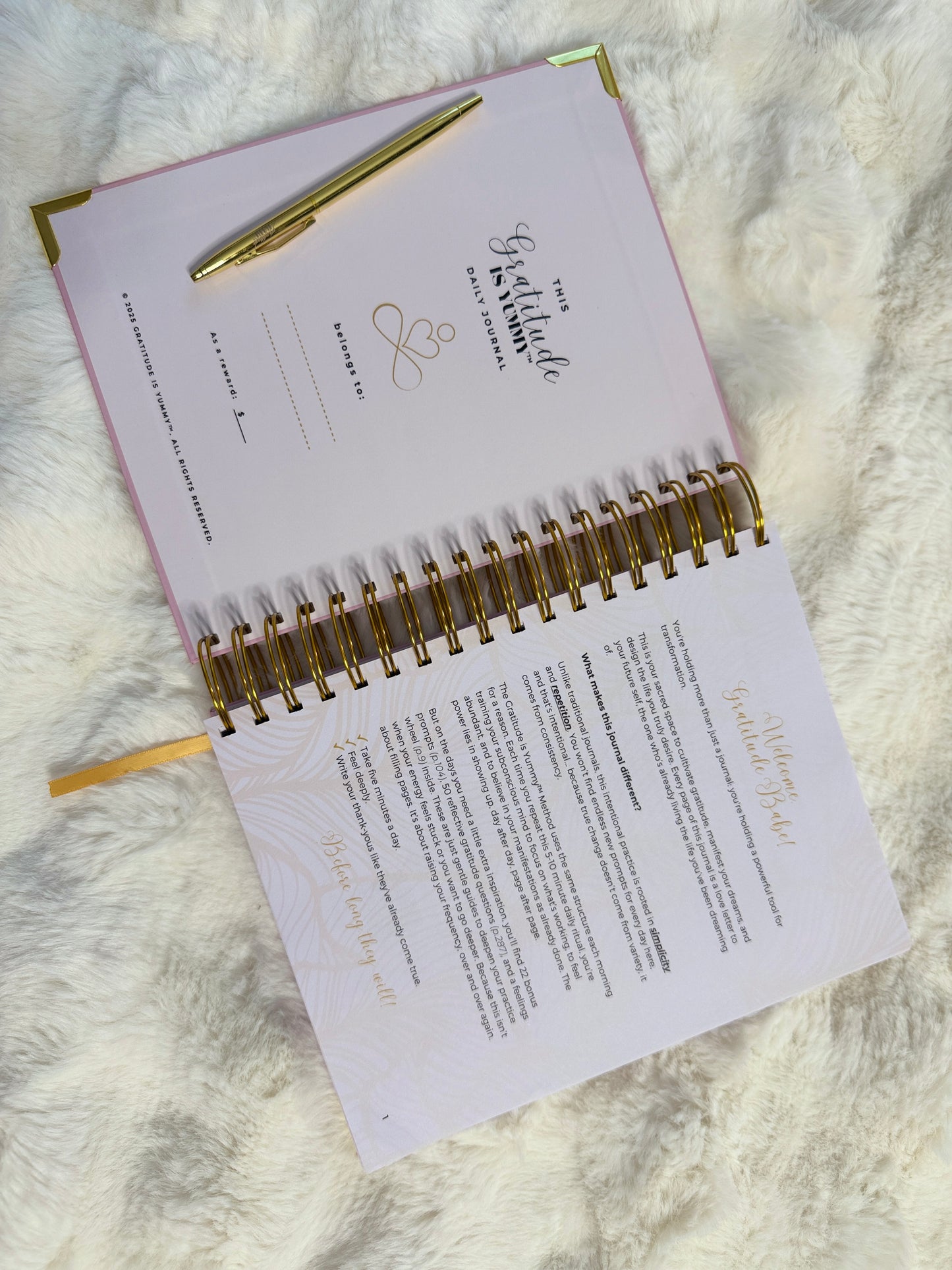 Pink planner with gold spiral binding and pen on a white fur surface