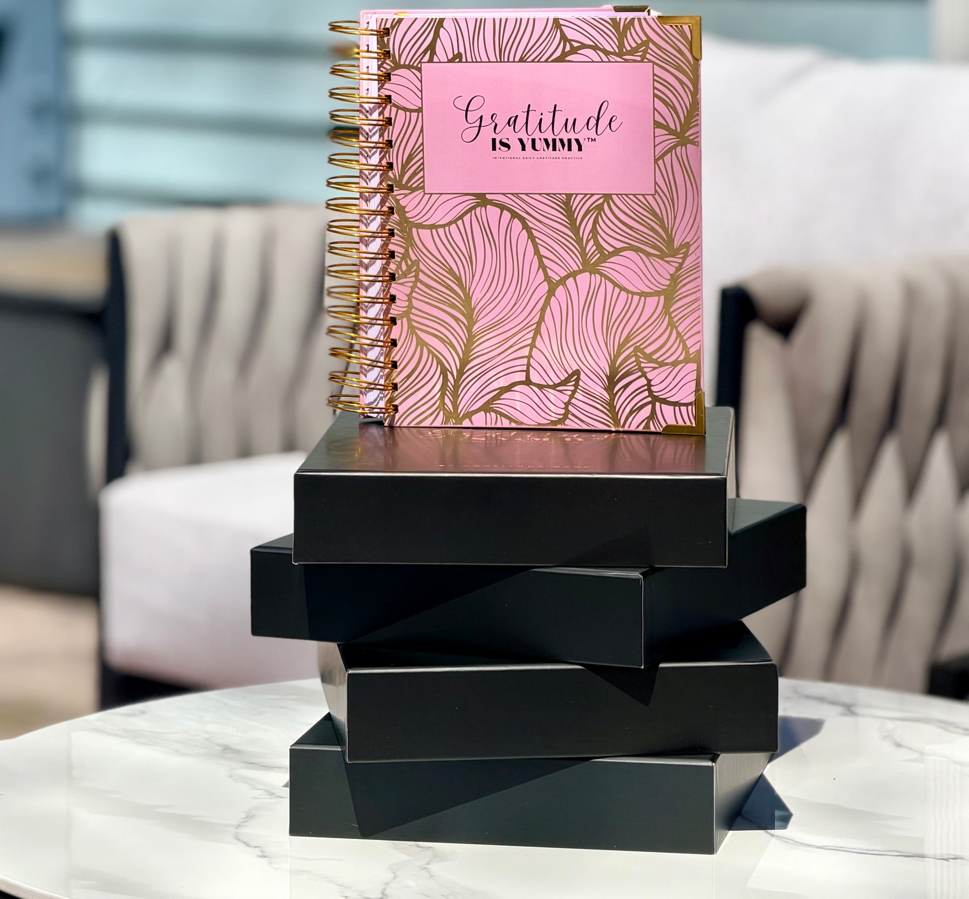 Blush pink spiral journal with gold foil, with 'Gratitude is Yummy' on a a stack of black gift boxes. Pink. Girly. Aesthetic. Mindset. Manifestation. outdoor. Gratitude journal. Manifestation journal. Gratitude manifestation journal. 