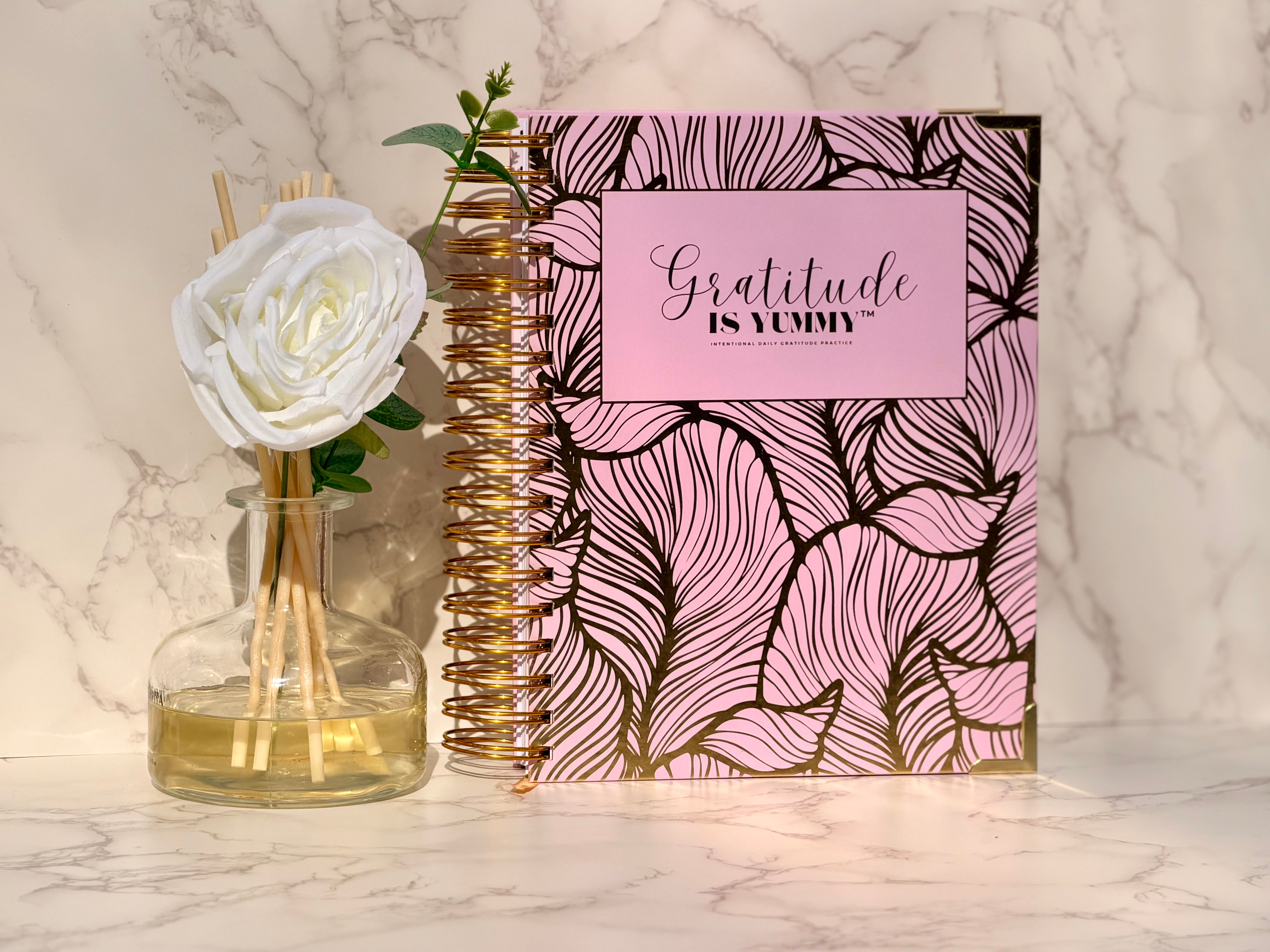 Physical Gratitude is Yummy Journal with blush pink cover, gold accents, and white rose on a marble surface for a five-minute gratitude ritual