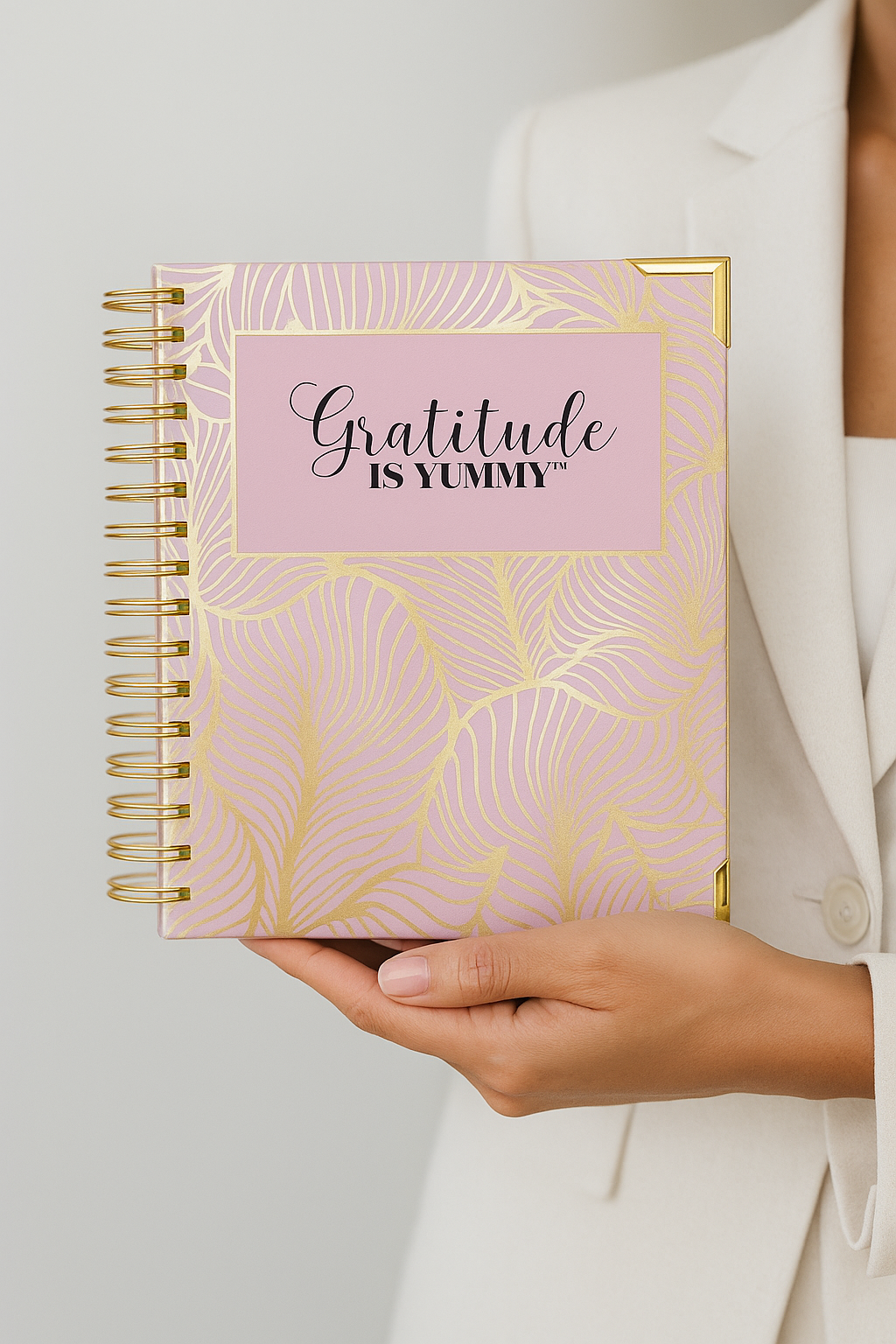 Person holding a pink notebook with 'Gratitude is Yummy' text and gold accents.