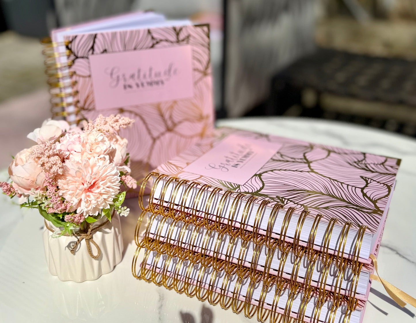Stack of Blush pink spiral journal with gold foil, with 'Gratitude is Yummy' on a marble surface outdoor with a gratitude babe engraved gold pen. Pink. Girly. Aesthetic. Mindset. Manifestation