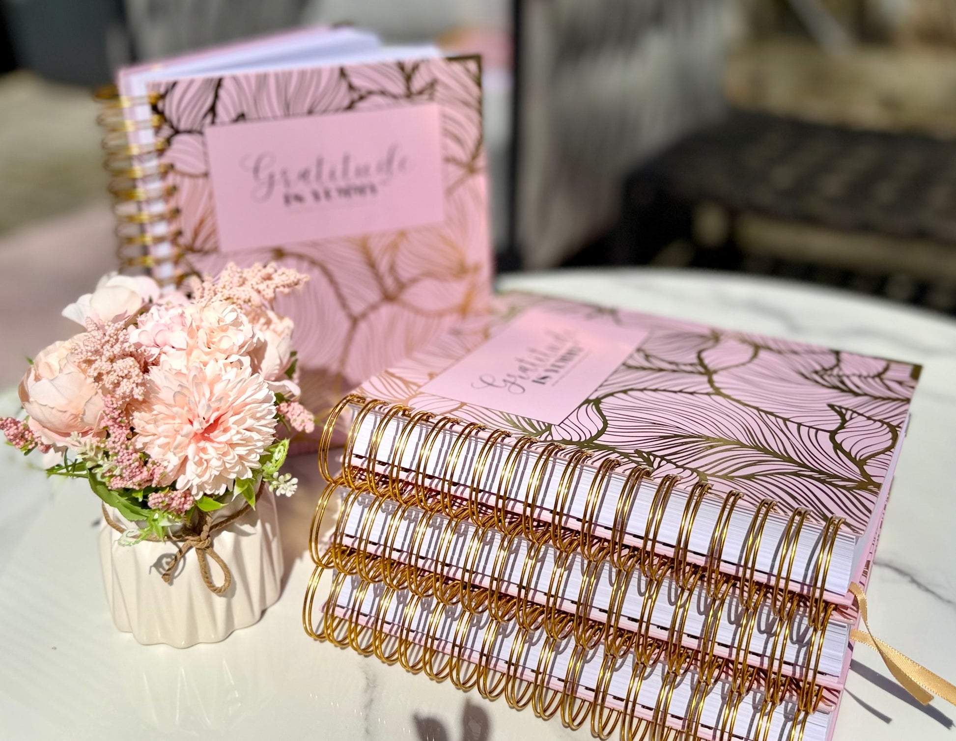 Stack of Blush pink spiral journal with gold foil, with 'Gratitude is Yummy' on a marble surface outdoor with a gratitude babe engraved gold pen. Pink. Girly. Aesthetic. Mindset. Manifestation
