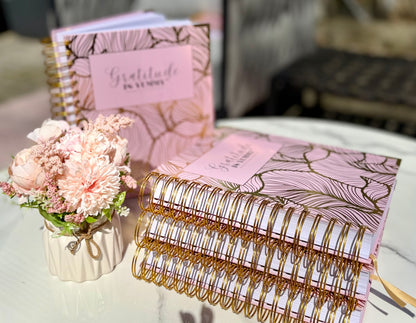 Stack of Blush pink spiral journal with gold foil, with 'Gratitude is Yummy' on a marble surface outdoor with a gratitude babe engraved gold pen. Pink. Girly. Aesthetic. Mindset. Manifestation