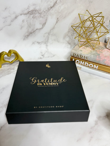 Black box with 'Gratitude is Yummy' text on a marble surface with decorative items.