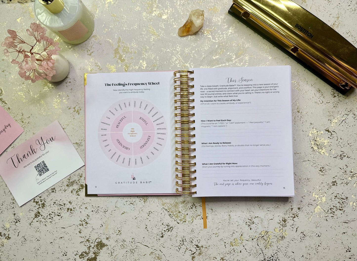 Open spiral-bound planner with pink cover on a textured surface with decorative elements.