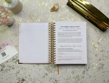 Open spiral-bound notebook on a textured surface with a pen and decorative items.