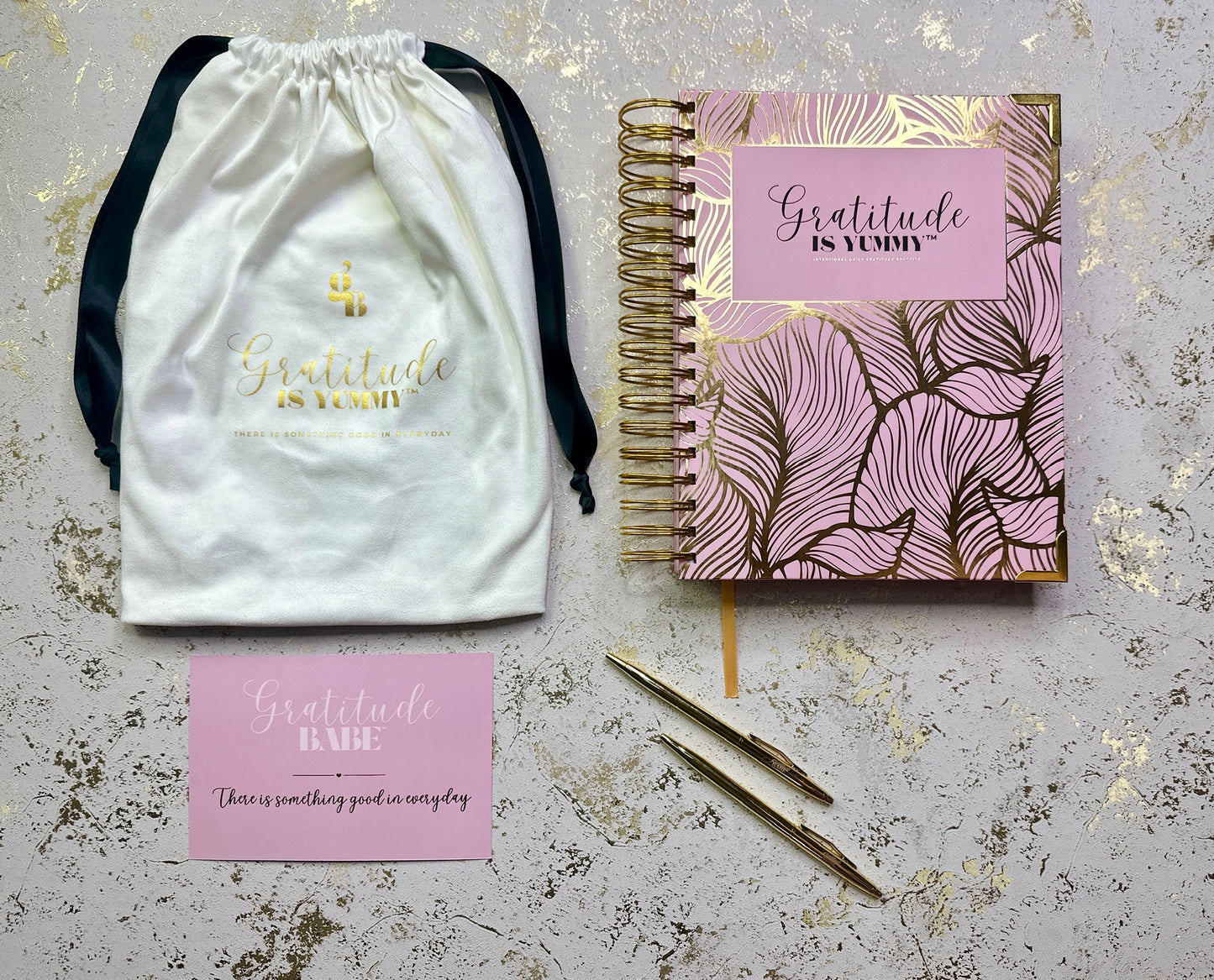 Product set with a drawstring bag, notebook, pen, and card on a textured surface.