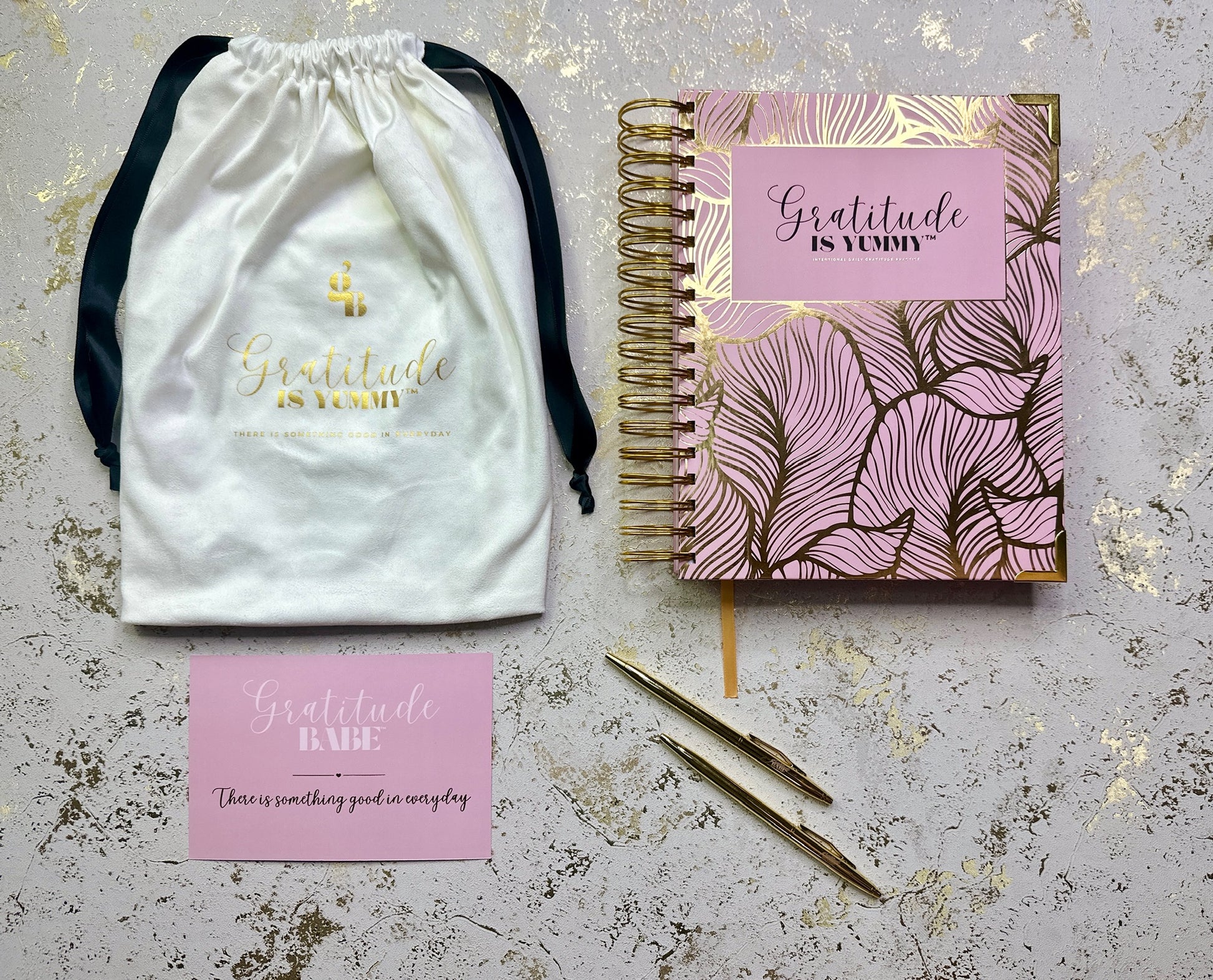 Product set with a drawstring bag, notebook, pen, and card on a textured surface.